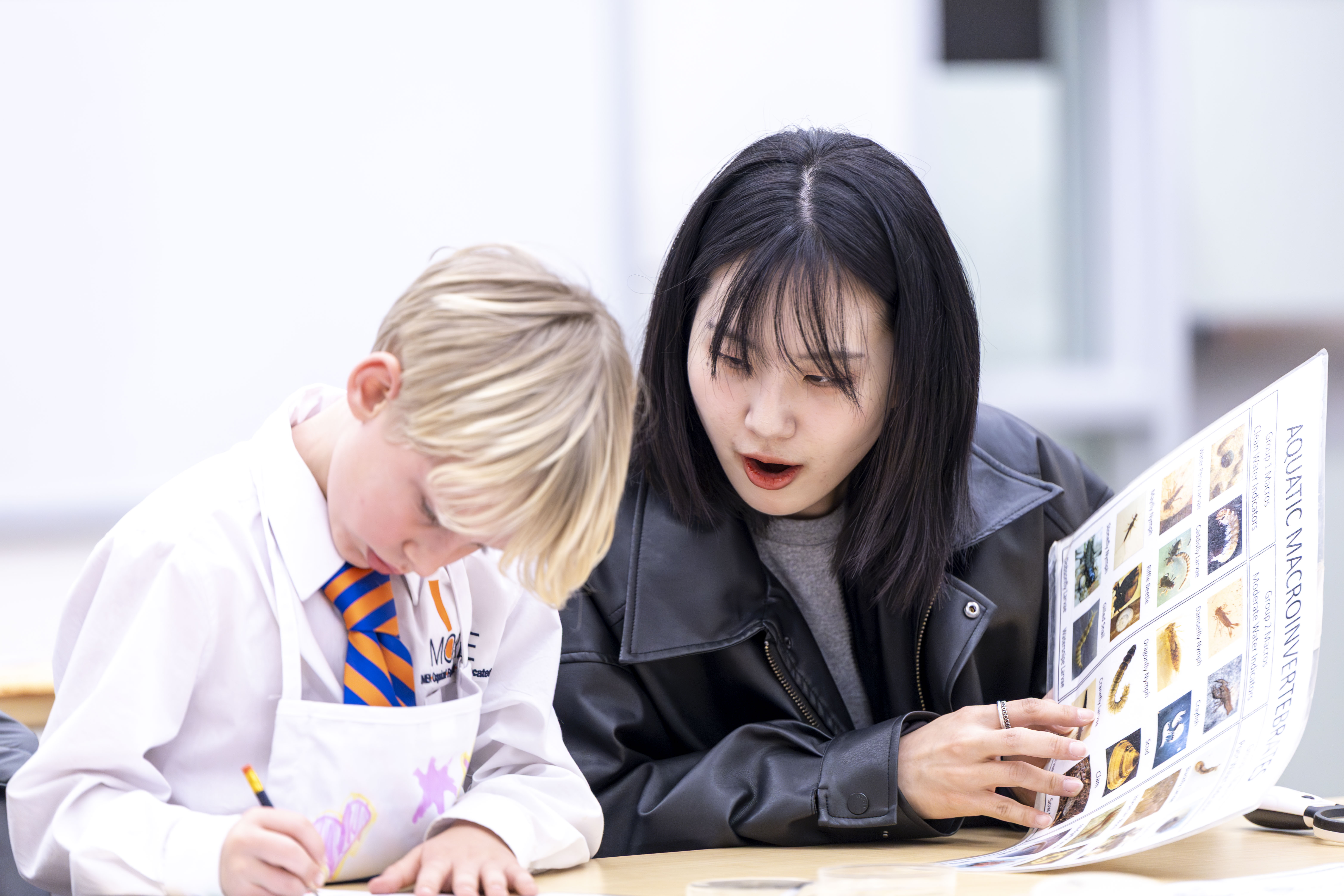 Asian female students teaching science to white male young student
